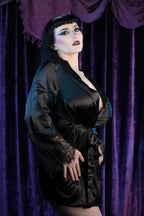 Model wearing Dahlia, seen from the side, a sexy black satin robe with black lace detailing on the cuffs